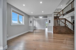 Recessed lighting illuminates the open-concept space, featuring light wood-finish flooring and a staircase with a dark wood-finish handrail and banister - 