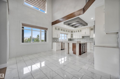 High ceilings with clerestory windows, white cabinetry, a kitchen island with a stone countertop, and white tile flooring - 9054 24 Avenue Sw, Edmonton, AB 