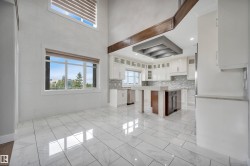 High ceilings with clerestory windows, white cabinetry, a kitchen island with a stone countertop, and white tile flooring - 