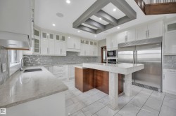 Gourmet kitchen with white cabinetry, stainless steel appliances, a tiled backsplash, a central island with a waterfall countertop, and recessed lighting - 