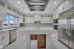 Kitchen featuring white cabinetry with glass inserts, stainless steel appliances, a large center island with a waterfall countertop, a tiled backsplash, and recessed lighting - 