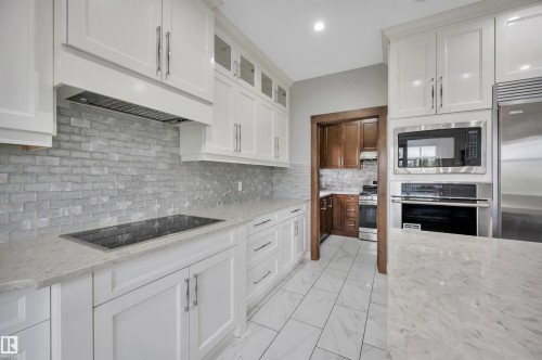White shaker cabinetry, light-toned countertops, a tile backsplash, integrated cooktop, and stainless steel appliances - 9054 24 Avenue Sw, Edmonton, AB 