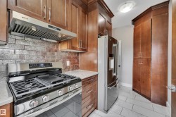 Kitchen featuring wood cabinetry, stainless steel appliances, stone countertops, a tile backsplash, and tile flooring - 