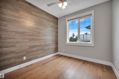 Wood-plank accent wall, wood-finish flooring, white window trim, and ceiling fan with light fixture - 9054 24 Avenue Sw, Edmonton, AB 