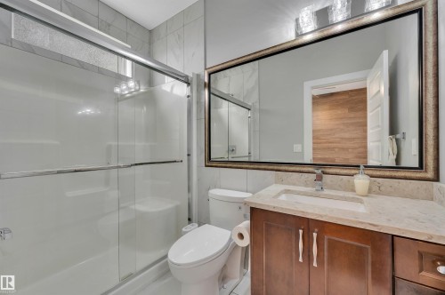 Full wall vanity mirror with decorative frame, wood-finish cabinetry, stone countertop, and a shower-tub combination with sliding glass doors - 9054 24 Avenue Sw, Edmonton, AB 