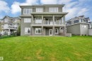 Expansive green lawn with a two-story stucco exterior, upper-level covered balcony with white railings, ground-level patio, and stone column detailing - 9054 24 Avenue Sw, Edmonton, AB 