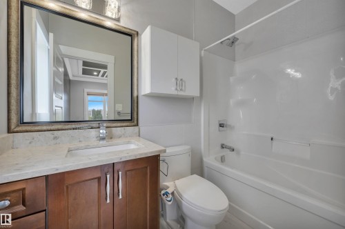 Wood-finish vanity with an undermount sink, light-toned countertop, and framed mirror - 9054 24 Avenue Sw, Edmonton, AB 