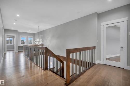 Wood-finish flooring, staircase with wood railing and metal spindles, recessed lighting, white trim, and a contemporary chandelier - 9054 24 Avenue Sw, Edmonton, AB 
