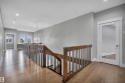 Wood-finish flooring, staircase with wood railing and metal spindles, recessed lighting, white trim, and a contemporary chandelier - 
