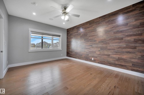 Wood-finish accent wall, light wood-finish flooring, recessed lighting, ceiling fan, and a large window - 9054 24 Avenue Sw, Edmonton, AB 