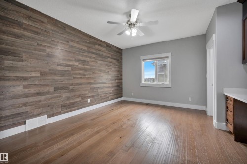 Wood-finish accent wall with coordinating wood-finish flooring, ceiling fan, and built-in cabinetry with a light-toned countertop - 9054 24 Avenue Sw, Edmonton, AB 