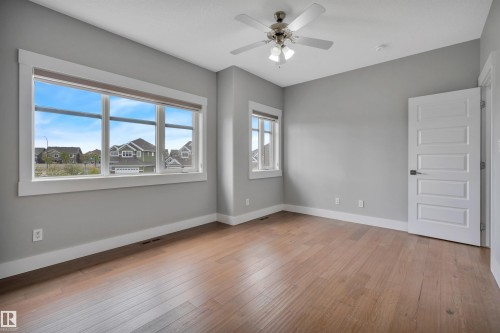 Wood-finish flooring, multiple large windows, neutral gray wall tones, contemporary white five-panel door, and a ceiling fan with integrated lighting - 9054 24 Avenue Sw, Edmonton, AB 