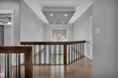 Wood-finish flooring, contemporary railing with dark wood and vertical metal balusters, and a tiered ceiling with recessed lighting - 9054 24 Avenue Sw, Edmonton, AB 