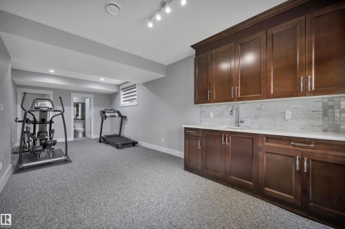 Expansive entertainment space with a wet bar featuring wood-finish cabinetry, a white countertop, and a tiled backsplash - 9054 24 Avenue Sw, Edmonton, AB 