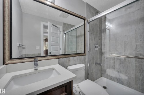Bathroom featuring a built-in vanity with an undermount sink, a framed mirror, a toilet, a tub, and a shower with a glass enclosure and tile surround - 9054 24 Avenue Sw, Edmonton, AB 
