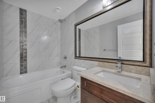 Bathroom featuring a built-in tub with tile surround, a vanity with an integrated sink, a framed mirror, and a chrome faucet - 9054 24 Avenue Sw, Edmonton, AB 