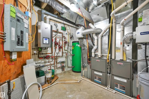 Utility room featuring a circuit breaker panel, wall-mounted water heater, comprehensive plumbing system, and dual furnaces - 9054 24 Avenue Sw, Edmonton, AB 