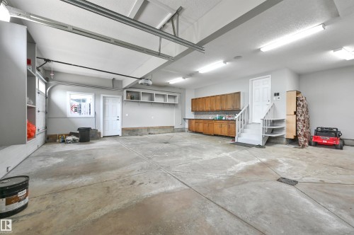 Spacious garage featuring concrete flooring, built-in wooden cabinetry, recessed wall shelving, and overhead fluorescent lighting - 9054 24 Avenue Sw, Edmonton, AB 