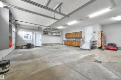 Spacious garage featuring concrete flooring, built-in wooden cabinetry, recessed wall shelving, and overhead fluorescent lighting - 