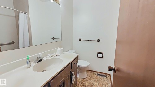 Vanity with integrated sink, wood-finish cabinetry, wall-mounted mirror, and patterned flooring - 3031 79 Street Nw, Edmonton, AB 