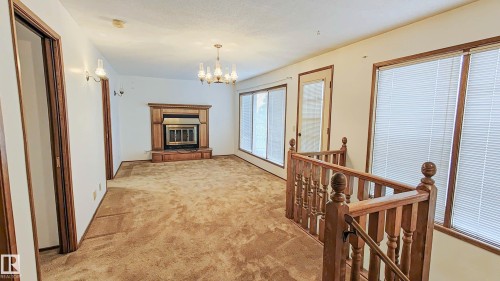 Living space with a fireplace, chandelier, and wood-finish banister - 3031 79 Street Nw, Edmonton, AB 