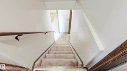 Staircase featuring carpeted treads, a wood handrail with dark metal supports, and neutral wall tones - 