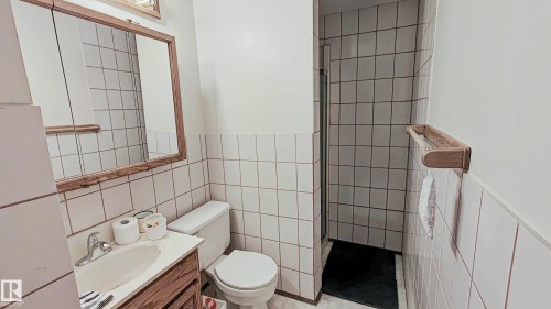 Compact bathroom featuring a shower stall, white tiled walls, wood-finish vanity, and a mirrored medicine cabinet - 3031 79 Street Nw, Edmonton, AB 