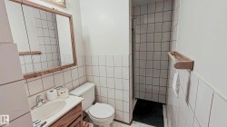 Compact bathroom featuring a shower stall, white tiled walls, wood-finish vanity, and a mirrored medicine cabinet - 