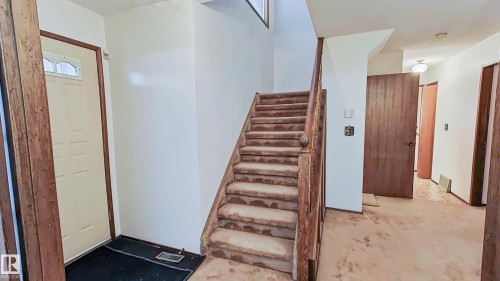 Two-story entryway featuring wood trim, a paneled front door with decorative glass, and a carpeted staircase with a wood handrail - 3031 79 Street Nw, Edmonton, AB 