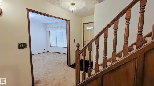 Entry area featuring a solid wood staircase with turned balusters, a front door with decorative glass, and a recessed room with bay windows - 3031 79 Street Nw, Edmonton, AB 