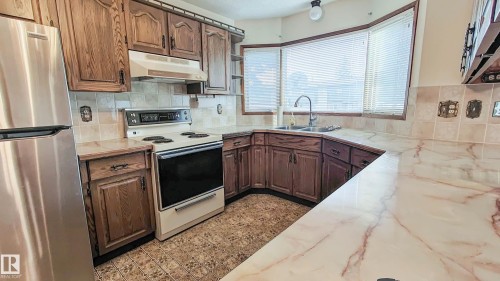 Kitchen featuring wood cabinetry, stainless steel refrigerator, white range, tile backsplash, and light-toned countertops - 3031 79 Street Nw, Edmonton, AB 