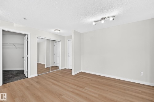 Wood-finish flooring, mirrored sliding closet doors, ceiling-mounted track lighting, and a flush-mount overhead light fixture - #1303 330 Clareview Station Dr Nw, Edmonton, AB 