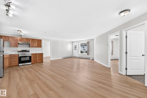 Open-concept living space featuring wood-finish flooring, recessed lighting, and a kitchen with wood cabinetry, stainless steel appliances, and white countertops - #1303 330 Clareview Station Dr Nw, Edmonton, AB 