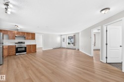 Open-concept living space featuring wood-finish flooring, recessed lighting, and a kitchen with wood cabinetry, stainless steel appliances, and white countertops - 