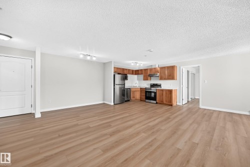 Open-concept living space featuring wood-finish flooring, recessed lighting, and a kitchen with stainless steel appliances, wood cabinetry, and white countertops - #1303 330 Clareview Station Dr Nw, Edmonton, AB 