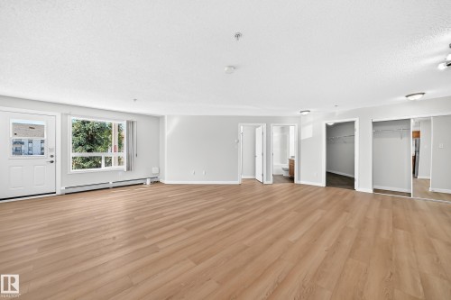 Expansive open-concept room featuring wood-finish flooring, a large window, a white entry door, and multiple closet spaces with mirrored sliding doors - #1303 330 Clareview Station Dr Nw, Edmonton, AB 