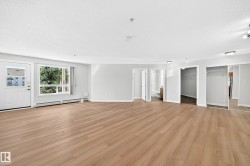 Expansive open-concept room featuring wood-finish flooring, a large window, a white entry door, and multiple closet spaces with mirrored sliding doors - 