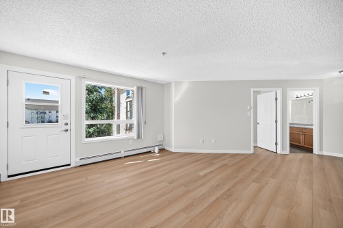 Expansive room featuring wood-finish flooring, white walls, multiple windows, and a white entry door - #1303 330 Clareview Station Dr Nw, Edmonton, AB 