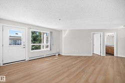 Expansive room featuring wood-finish flooring, white walls, multiple windows, and a white entry door - 