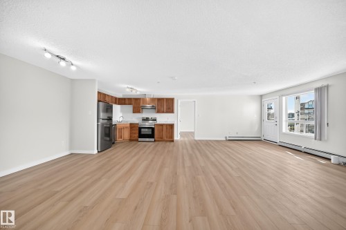 Open-concept living space featuring wood-finish flooring, a kitchen with stainless steel appliances, wood cabinetry, and track lighting, and a window providing natural illumination - #1303 330 Clareview Station Dr Nw, Edmonton, AB 