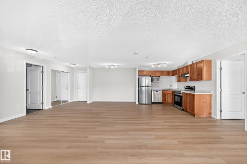 Open-concept living area with wood-finish flooring, recessed lighting, and a kitchen featuring stainless steel appliances and wood cabinetry - #1303 330 Clareview Station Dr Nw, Edmonton, AB 