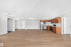 Open-concept living area with wood-finish flooring, recessed lighting, and a kitchen featuring stainless steel appliances and wood cabinetry - 