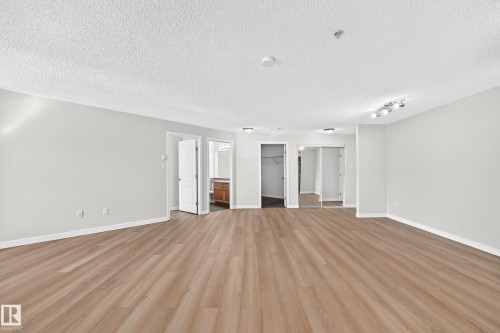 Spacious room featuring wood-finish flooring, light gray walls, and track lighting - #1303 330 Clareview Station Dr Nw, Edmonton, AB 