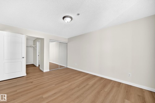 Wood-finish flooring with neutral wall tones, a ceiling-mounted light fixture, and mirrored sliding closet doors - #1303 330 Clareview Station Dr Nw, Edmonton, AB 