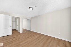 Wood-finish flooring with neutral wall tones, a ceiling-mounted light fixture, and mirrored sliding closet doors - 