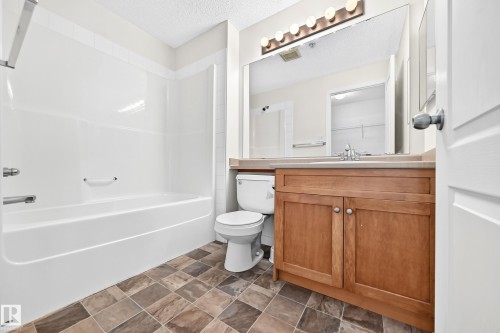 Spa-inspired bathroom featuring a wood-finish vanity with dual cabinet storage, ceramic countertop, and framed mirror with integrated lighting - #1303 330 Clareview Station Dr Nw, Edmonton, AB 