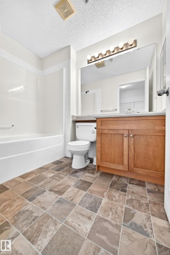 Tile flooring, wood-finish vanity, large vanity mirror, built-in bathtub with shower, and ceiling-mounted exhaust fan - #1303 330 Clareview Station Dr Nw, Edmonton, AB 
