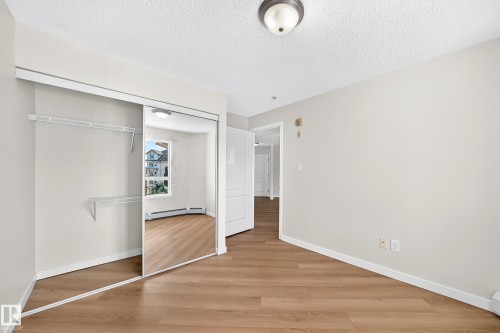 Wood-finish flooring, mirrored sliding closet doors, built-in closet shelving, and a semi-flush mount ceiling light - #1303 330 Clareview Station Dr Nw, Edmonton, AB 