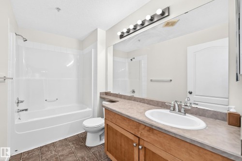 Full-size bathtub with shower, wood-finish vanity with an integrated sink, large wall-mounted mirror, and tile flooring - #1303 330 Clareview Station Dr Nw, Edmonton, AB 