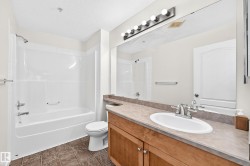 Full-size bathtub with shower, wood-finish vanity with an integrated sink, large wall-mounted mirror, and tile flooring - 